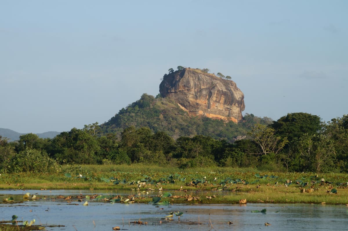 Sigiriya Rock Fortress rising above the lake and forest under a clear sky